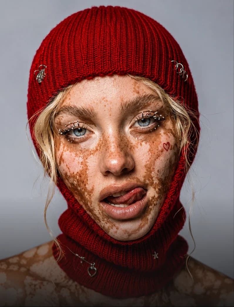 Mujer con pasamontañas rojo tejido y brillantina en la cara pecosa