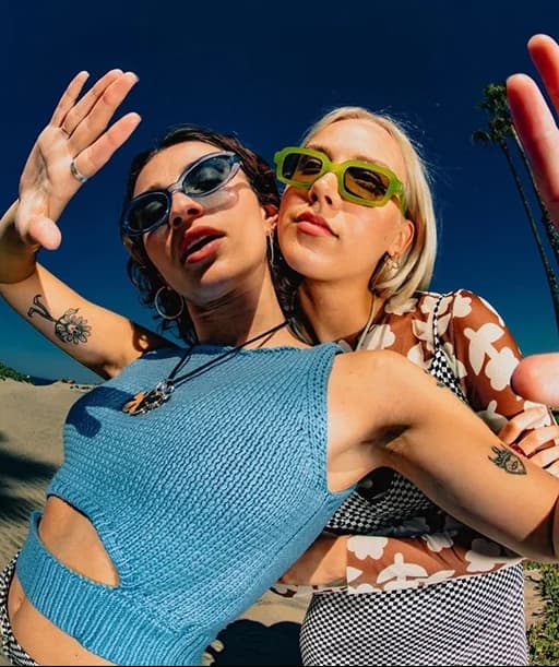 Dos mujeres con lentes de sol posando mejilla con mejilla bajo un cielo azul